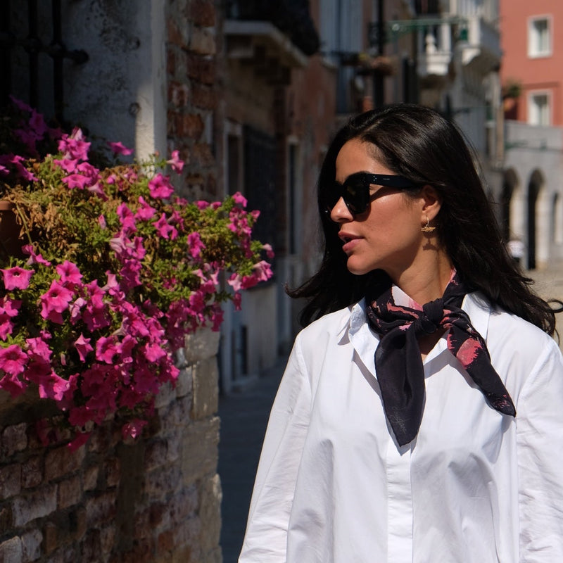 woman looking at flowers,  wearing wild bounty small silk square scarf in black and French pinks